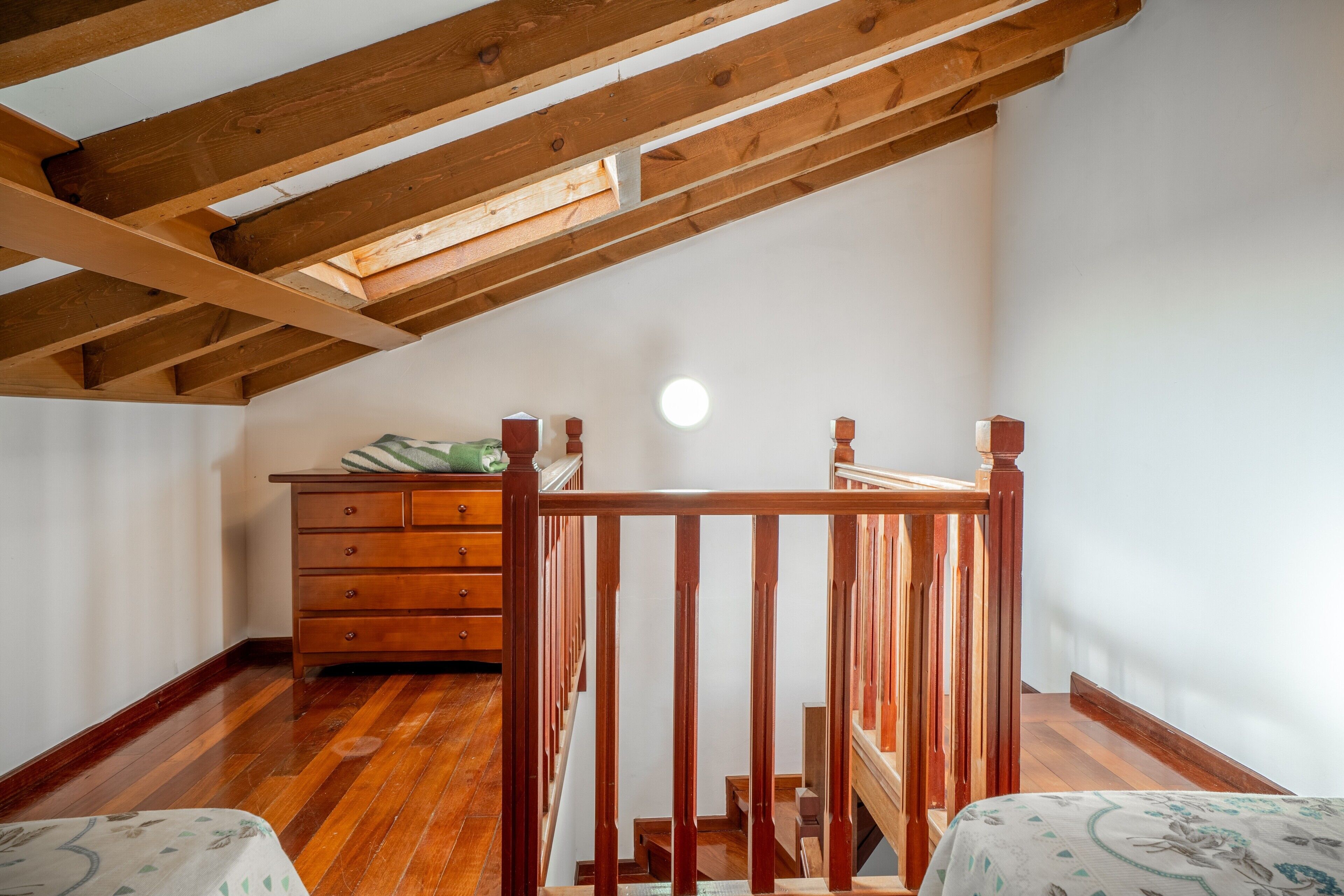 Una habitación con techo inclinado, vigas de madera, una escalera, un aparador y una cama.