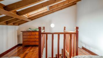 Una habitación con techo inclinado, vigas de madera, una escalera, un aparador y una cama.