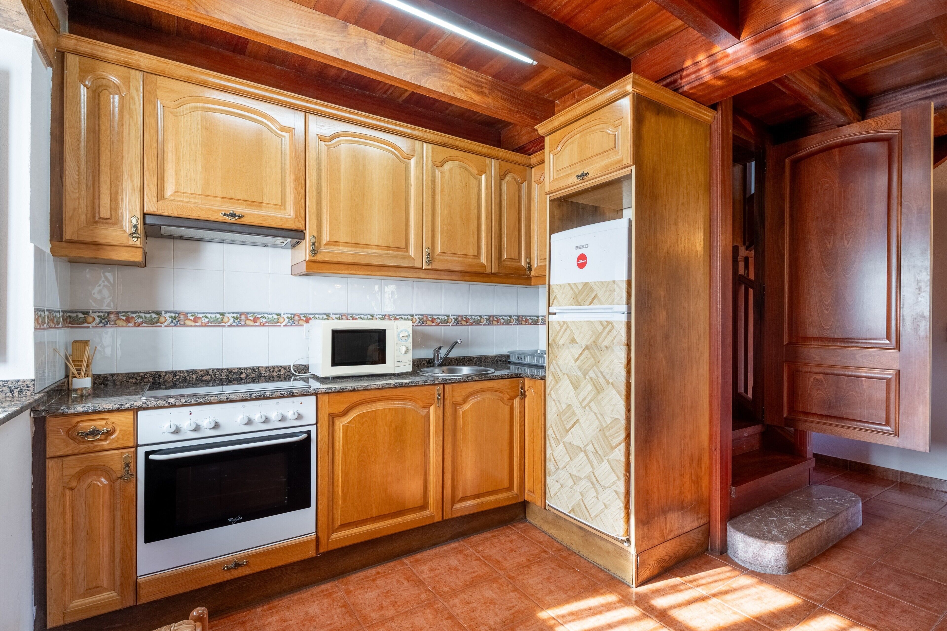Una cocina con armarios de madera, un microondas, un horno y un refrigerador.