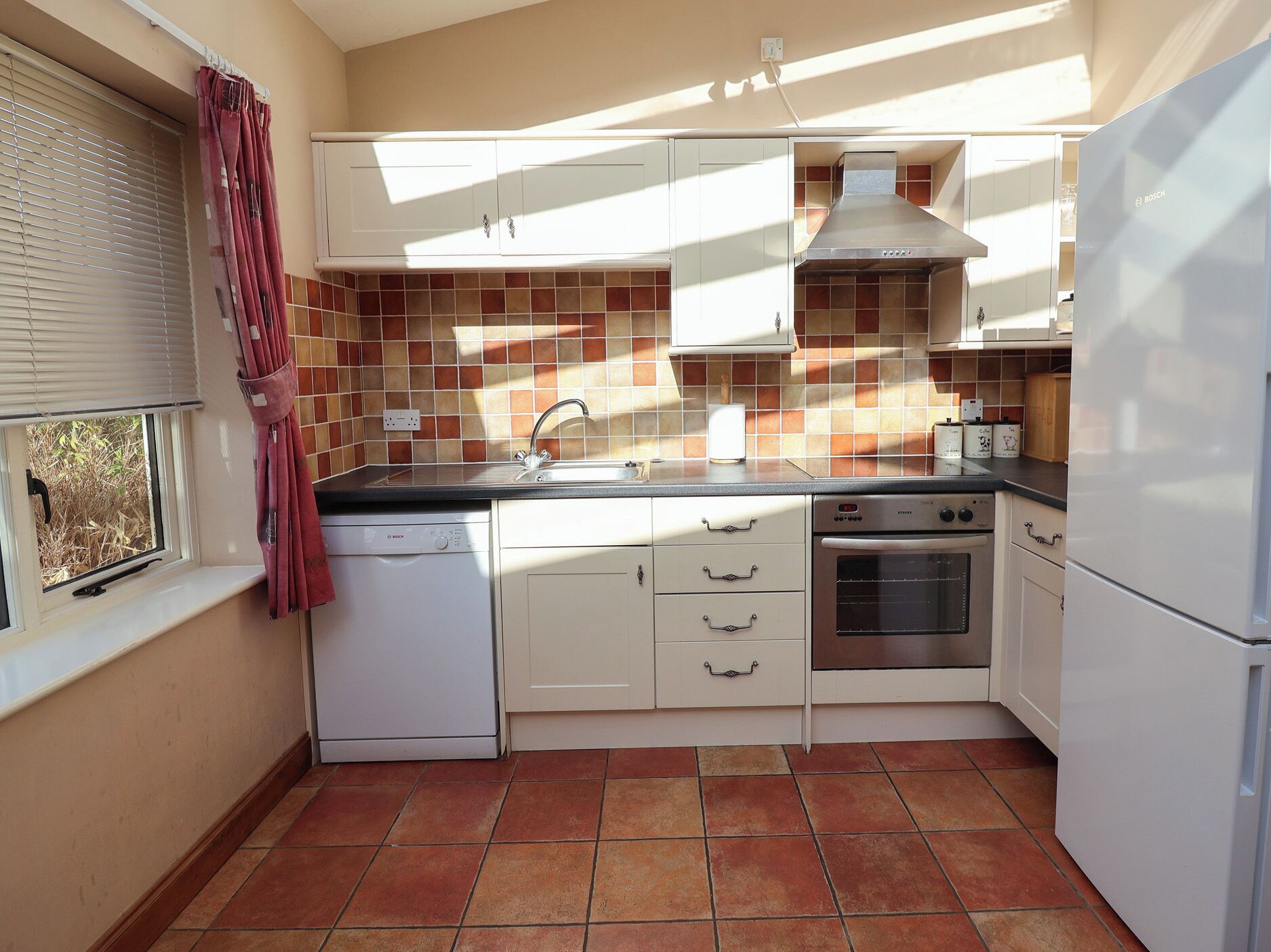 Cocina compacta con armarios blancos, lavavajillas Bosch, estufa y refrigerador.