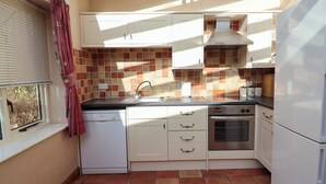 A compact kitchen with white cabinets, a Bosch dishwasher, a stove, and a refrigerator. - Wheelwright's Cottage (Ipswich)