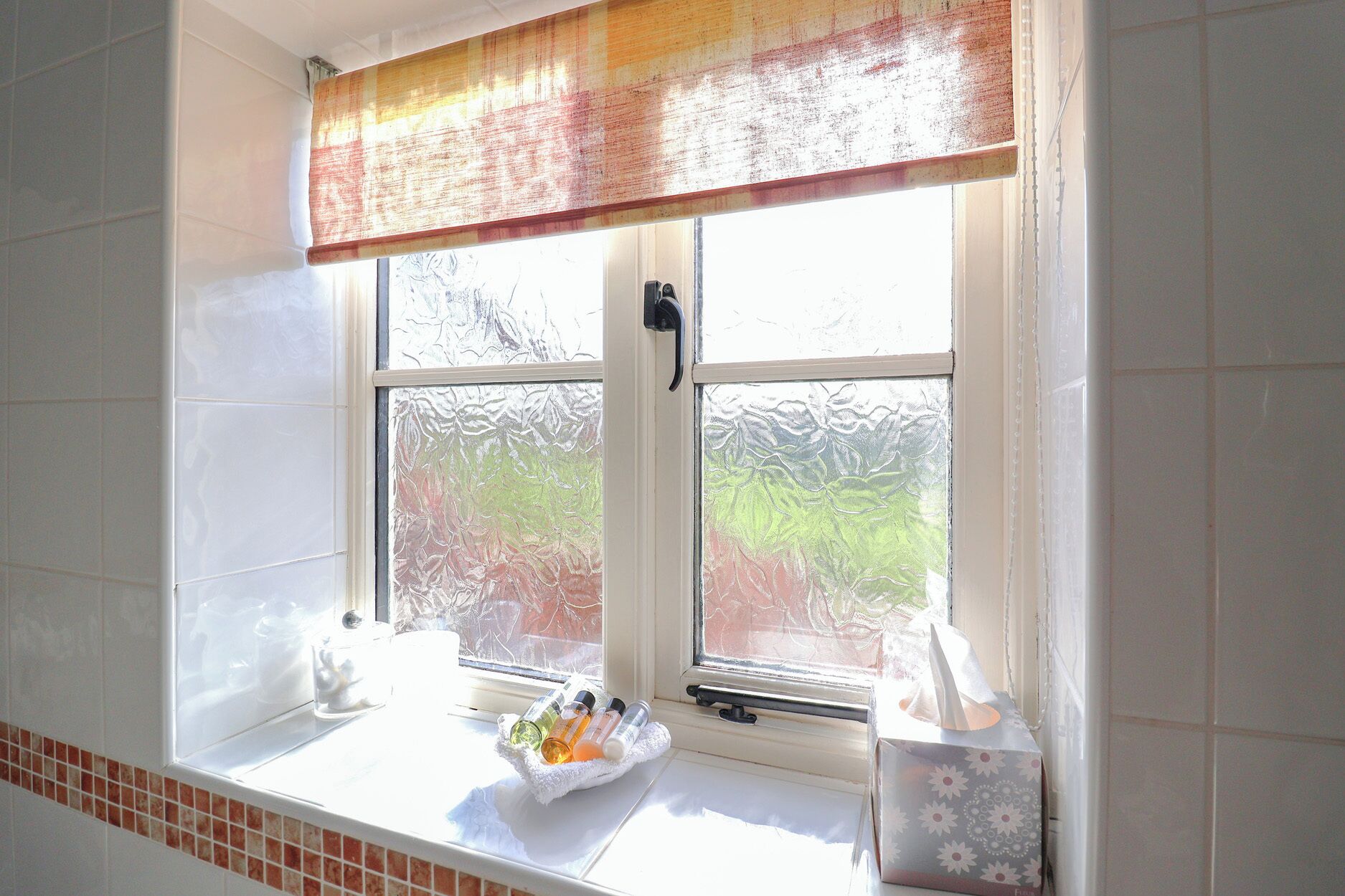 Un baño con ventana, un perchero y artículos de aseo sobre el alféizar.