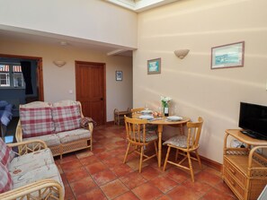 A cozy living room with a sofa, chairs, a dining table set for two, and a television on a stand. - Wheelwright's Cottage (Ipswich)