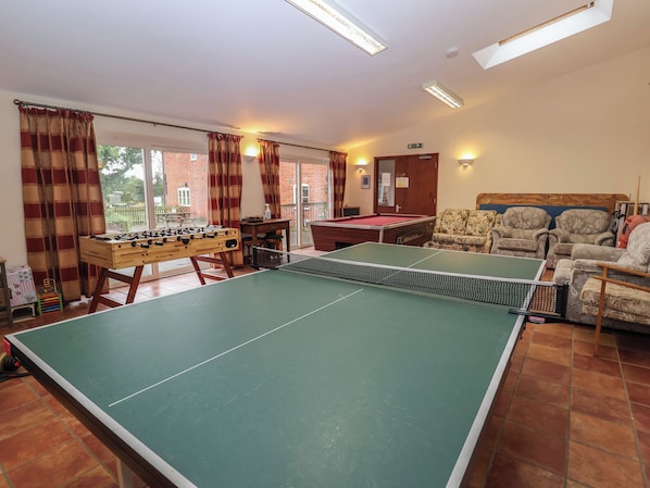 Une pièce équipée d’une table de ping-pong, d’un baby-foot et d’une table de billard. On y trouve quatre fauteuils et un canapé.