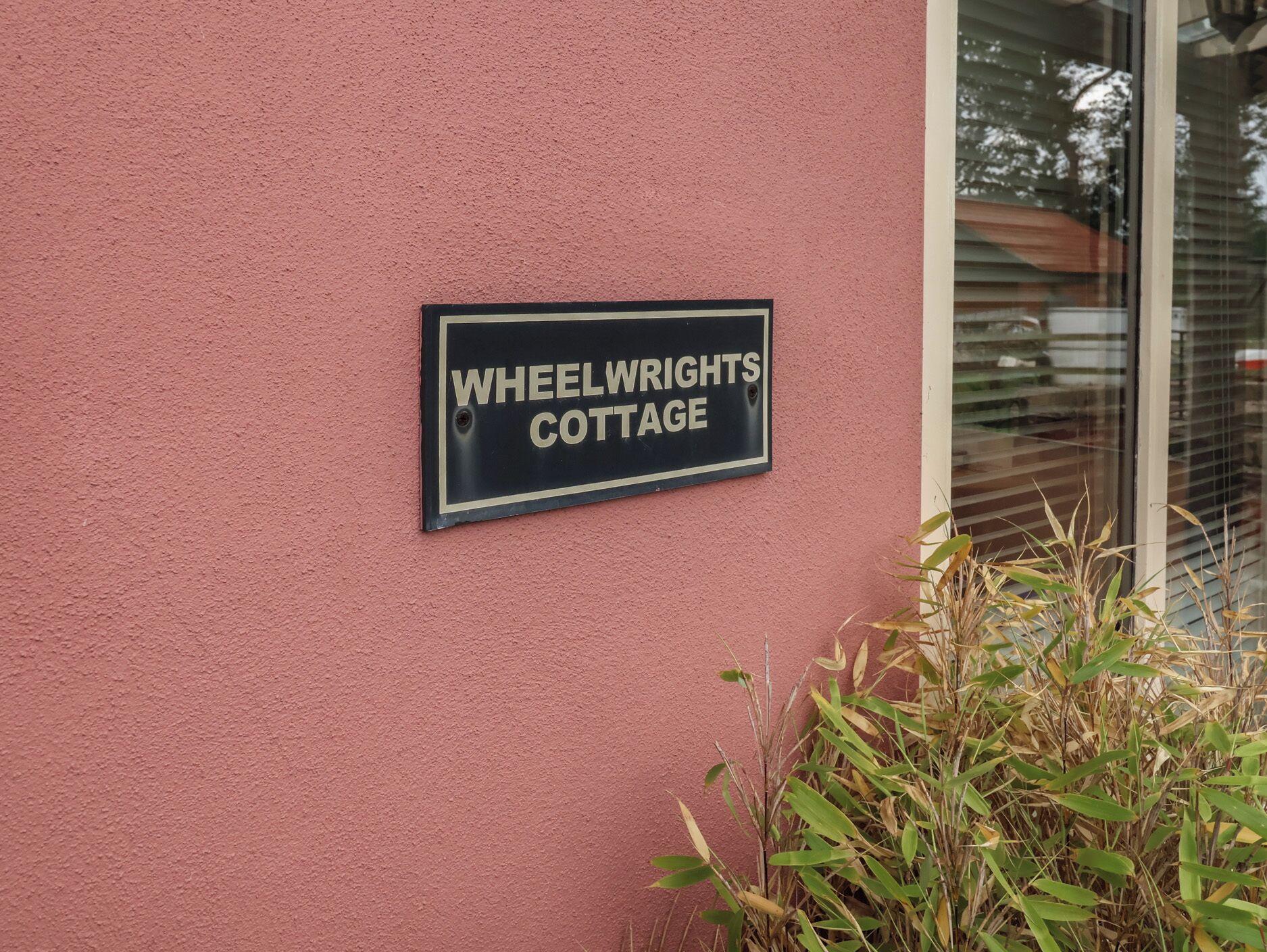 Un letrero en una pared rosa que dice 'WHEELWRIGHTS COTTAGE'.