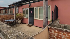A residential building with a red exterior, a black door, and a small patio area with a table and chairs. - Wheelwright's Cottage (Ipswich)
