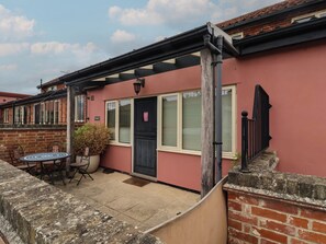 A residential building with a red exterior, a black door, and a small patio area with a table and chairs. - Wheelwright's Cottage (Ipswich)