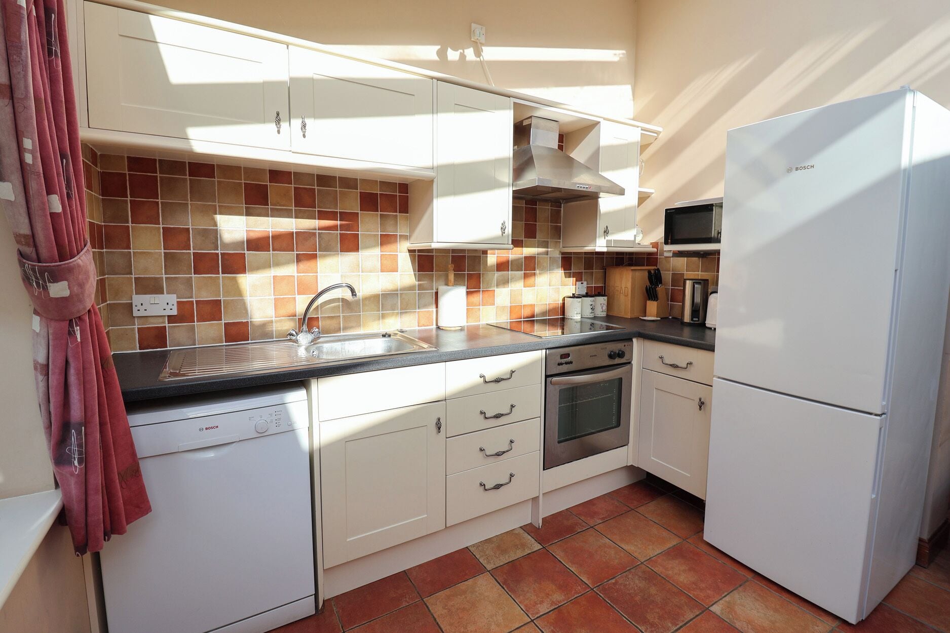 A compact kitchen with white cabinets, a stainless steel sink, a Bosch dishwasher, and a refrigerator.