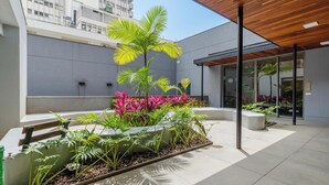 A modern outdoor space with a wooden ceiling, a seating area, and a variety of plants. - Aptos modernos em prédio com piscina a 300m do metrô - UOYs (São Paulo)