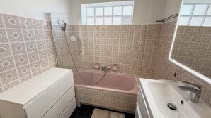 A bathroom with a bathtub, a sink, and a window.