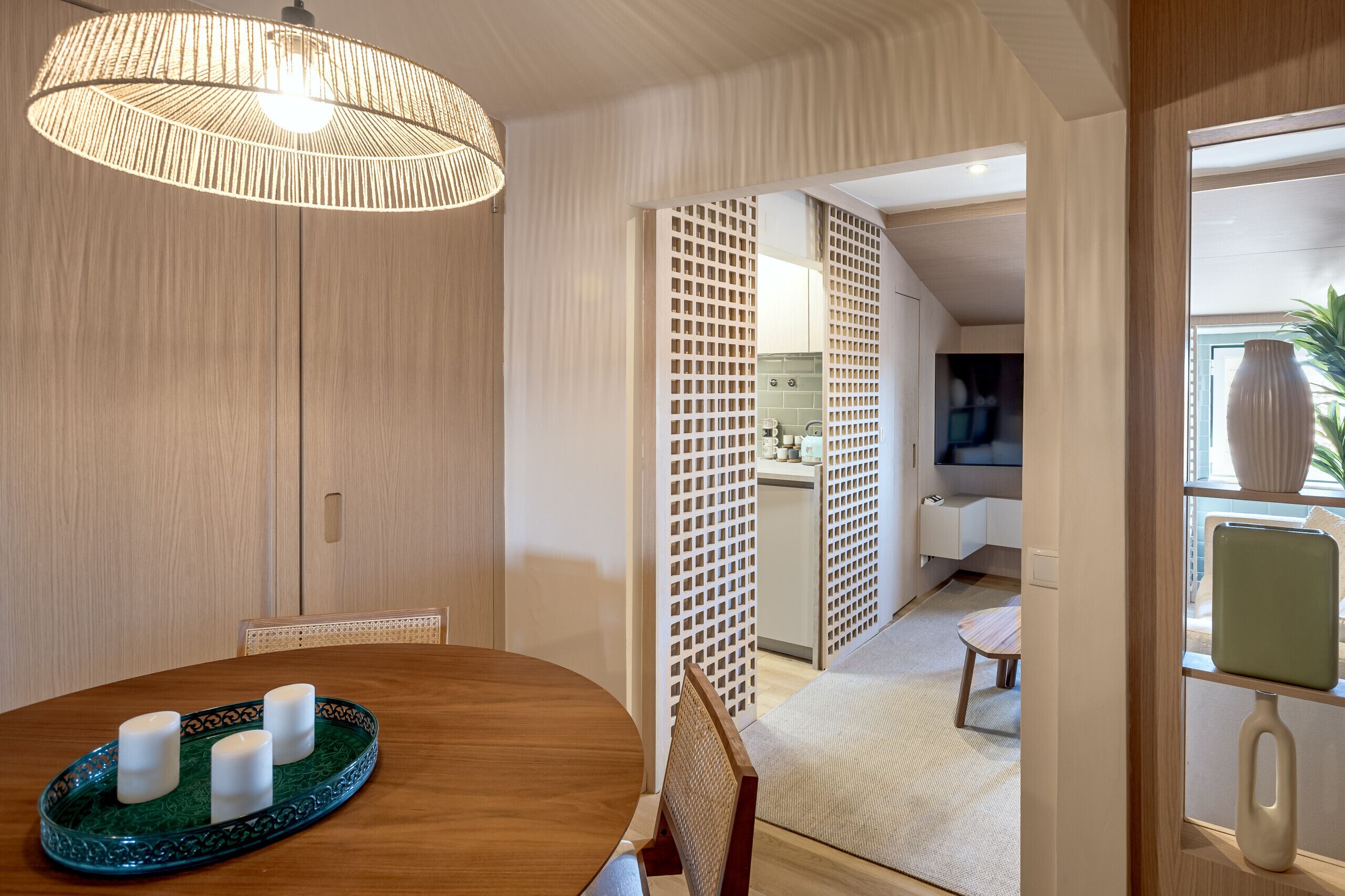 Uma sala de jantar com uma mesa de madeira, um tabuleiro verde com velas e uma luminária de fibra natural.