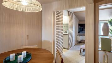 Uma sala de jantar com uma mesa de madeira, um tabuleiro verde com velas e uma luminária de fibra natural.
