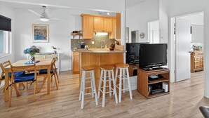 A modern kitchen with wooden cabinets, a dining area with a table and chairs, and a TV in the corner. - NEW! 1-bed condo in Carp, Steps to Sand! (Carpinteria)