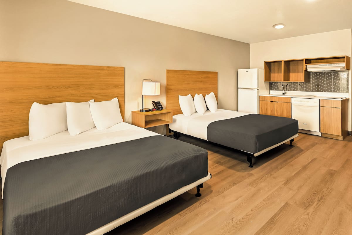 Une chambre d’hôtel avec deux lits, une kitchenette et un plancher en bois.