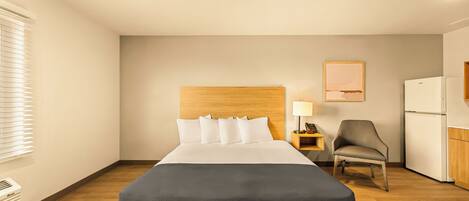 Une chambre d’hôtel avec un grand lit, une tête de lit en bois, un bureau avec une lampe, une chaise et un réfrigérateur.