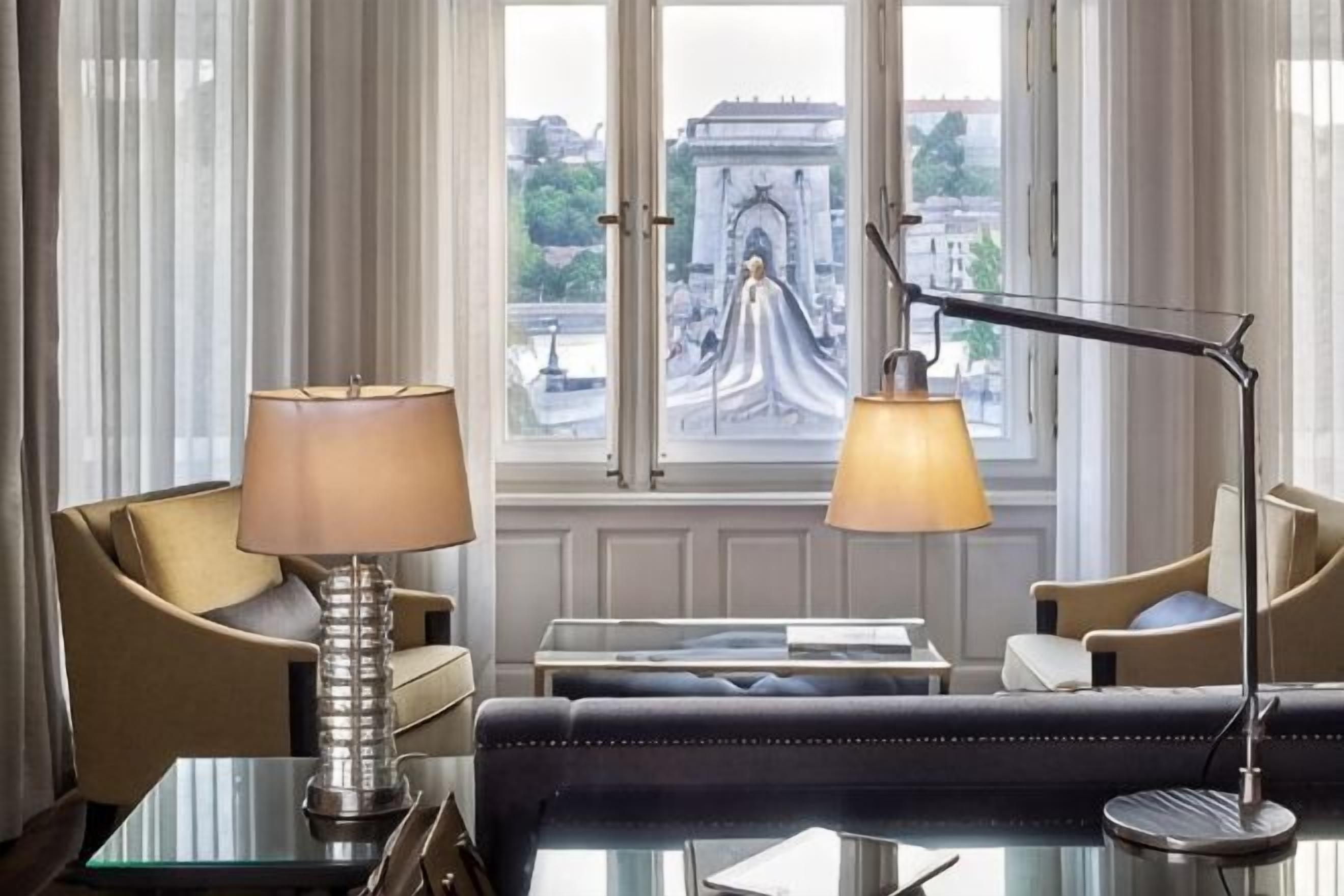 A room with a sofa, two lamps, a table, and a view of a historic building through a window.