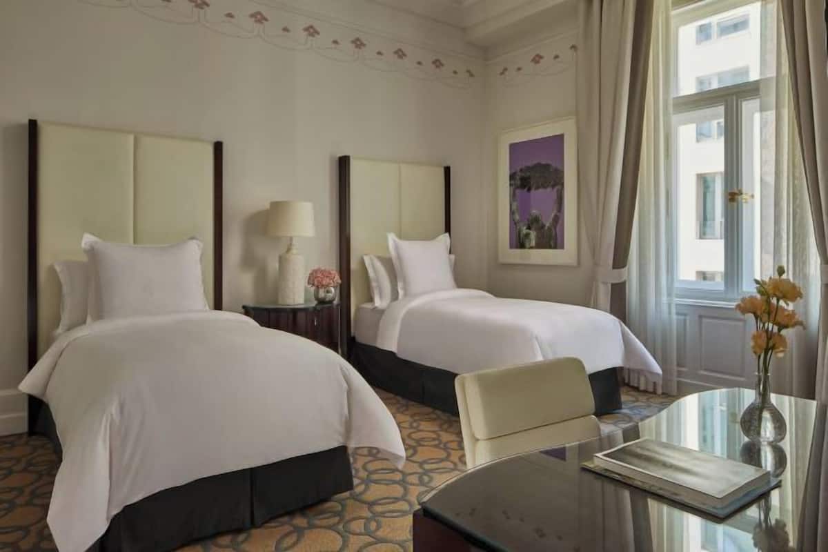Habitación de hotel con dos camas, una mesa de vidrio, un florero con flores y un cuadro en la pared.
