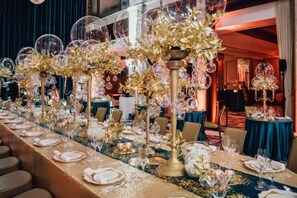 A long banquet table with a gold tablecloth, glassware, and floral centerpieces.