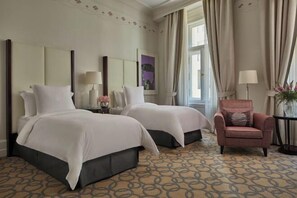 Habitación de hotel con dos camas, una silla, una lámpara y un ventanal con cortinas.