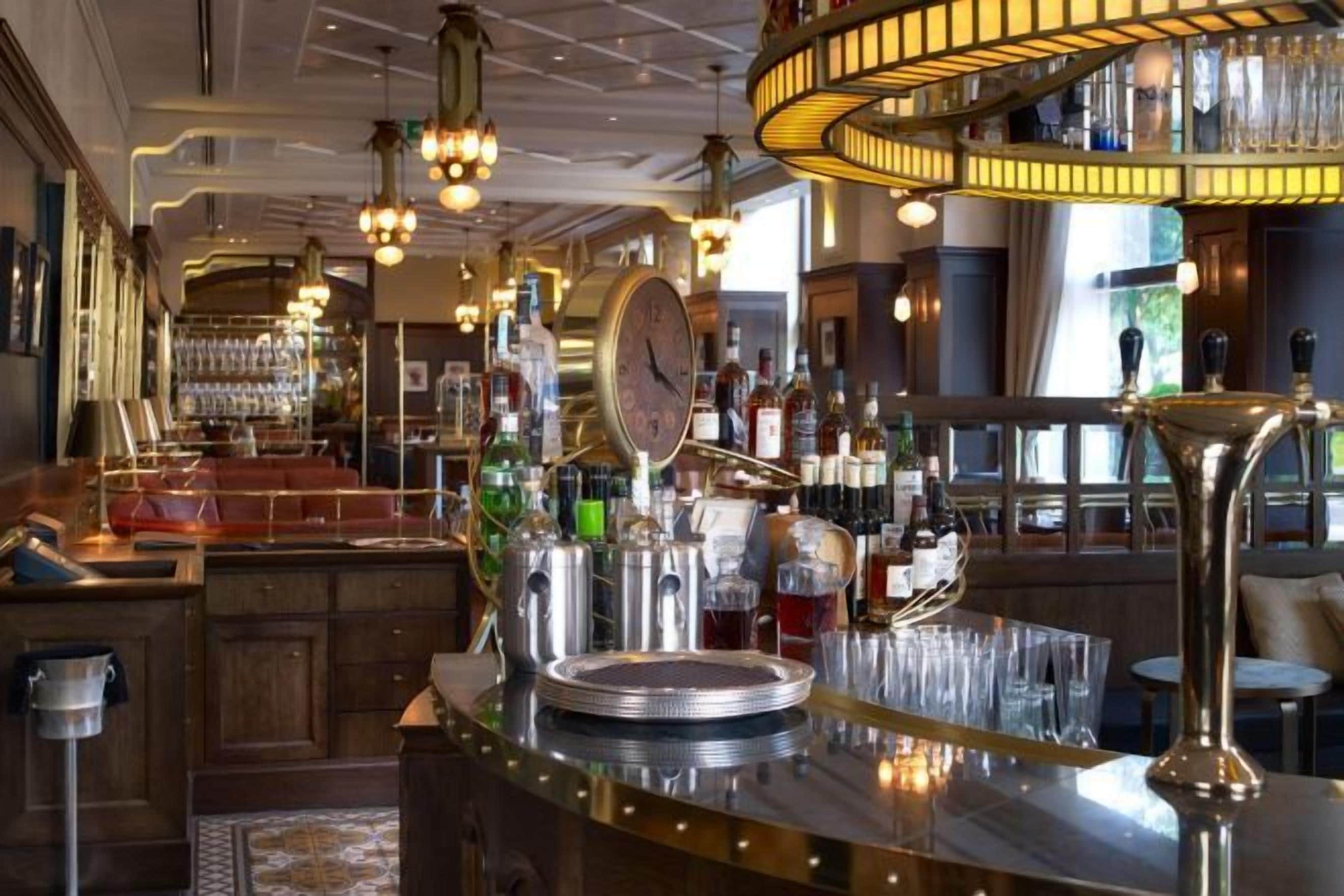 A bar area with a polished bar counter, various bottles, glasses, and a clock.