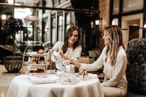 Deux personnes sont assises à une table, devant une variété de plats et un présentoir à gâteaux à plusieurs niveaux.