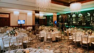 A banquet hall with round tables, chairs, and a chandelier.