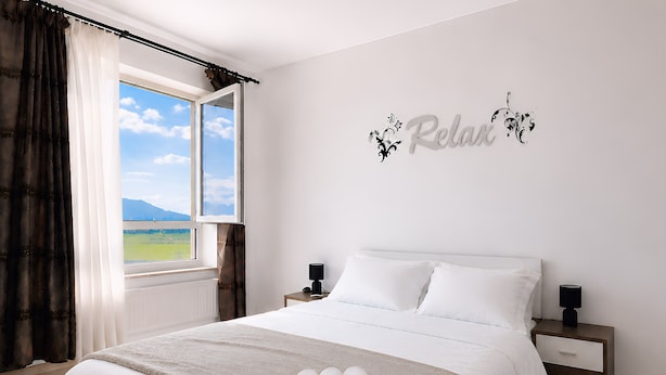 A bedroom with a bed, a nightstand, a wall decoration, and a window with curtains. - Brasov Altipiani Apartments (Brașov)