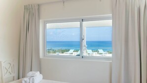 A hotel room with a bed, a window with a view of the sea and buildings, and a set of towels on the bed.