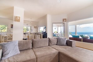 A modern living room with a large sectional sofa, a kitchen in the background, and a view of the ocean. - Bella Vista – Luxury Ocean View Villa with Private Pool & Daily Service (Coson, las terrenas, samana)