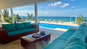 A poolside area with a wicker sofa, a glass coffee table, and a view of the ocean.