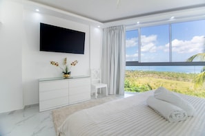 A modern bedroom with a large bed, a flat-screen TV, a white dresser, and a view of the ocean. - Bella Vista – Luxury Ocean View Villa with Private Pool & Daily Service (Coson, las terrenas, samana)