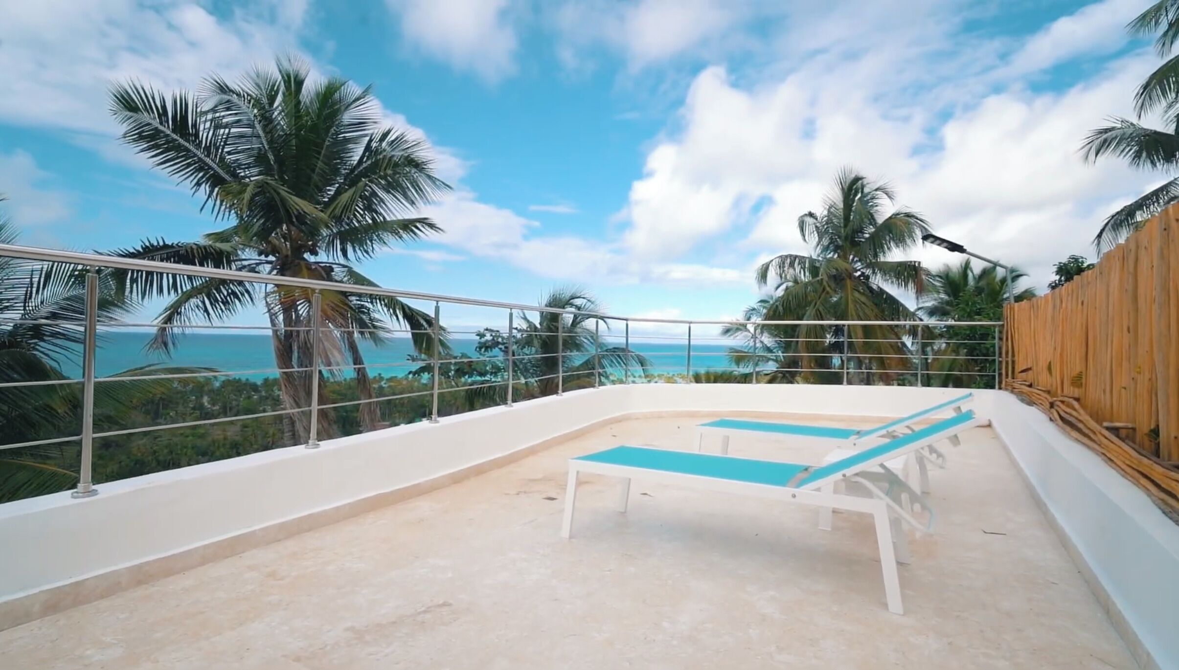 A balcony with a pool, palm trees, and a view of the ocean.