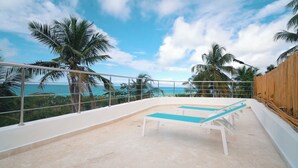 A balcony with a pool, palm trees, and a view of the ocean.