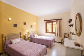 A room with two beds, a small table, a chair, a window with curtains, a mirror, and wall-mounted lights. - Townhouse Xisca Pollensa Majorca (Pollensa / Pollença)