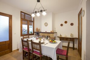 A dining area with a table set for four, surrounded by wooden chairs with pink cushions. A chandelier hangs above the table, and there are decorative plates on the wall. - Townhouse Xisca Pollensa Majorca (Pollensa / Pollença)