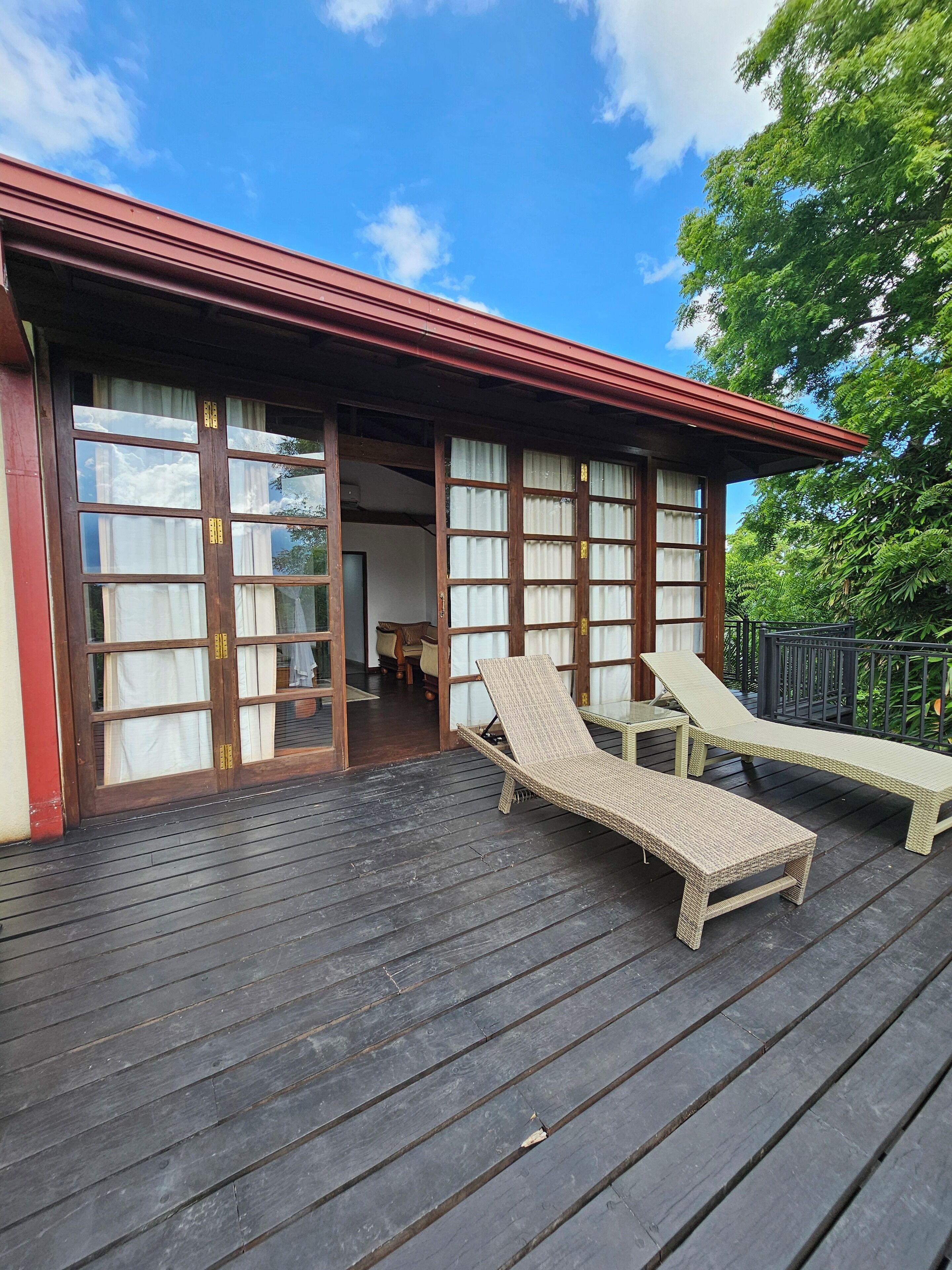 A wooden deck with two wicker lounge chairs and a building with large glass doors.