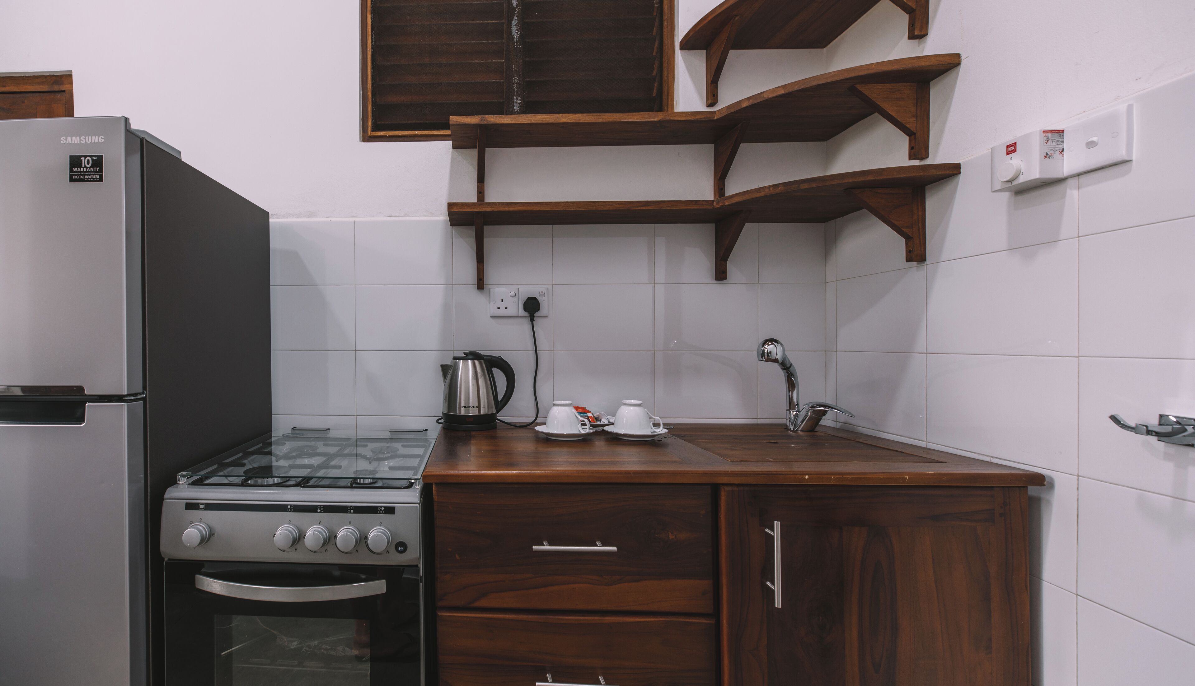 A kitchen with a stainless steel refrigerator, a gas stove, a kettle, two cups, and a sink.