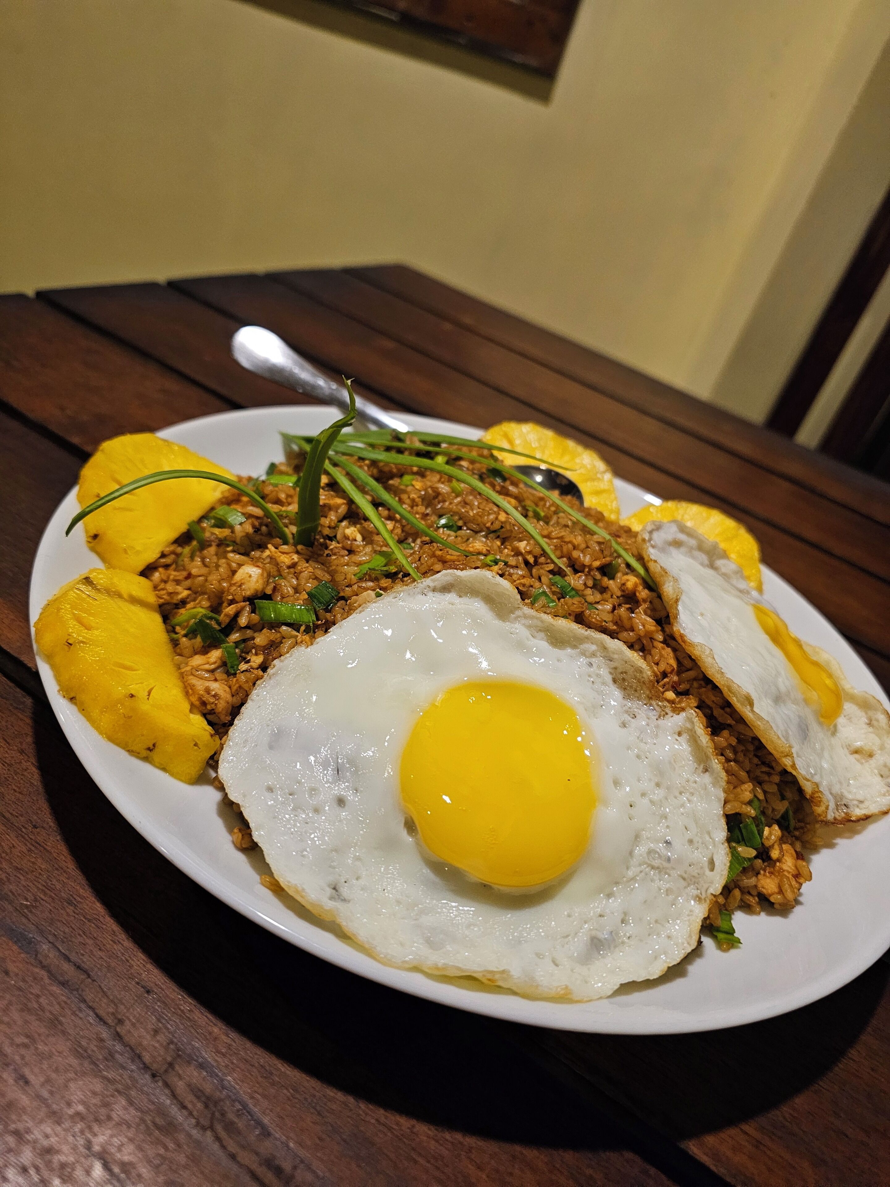 A plate of fried rice with a fried egg and slices of yellow fruit on a wooden table.