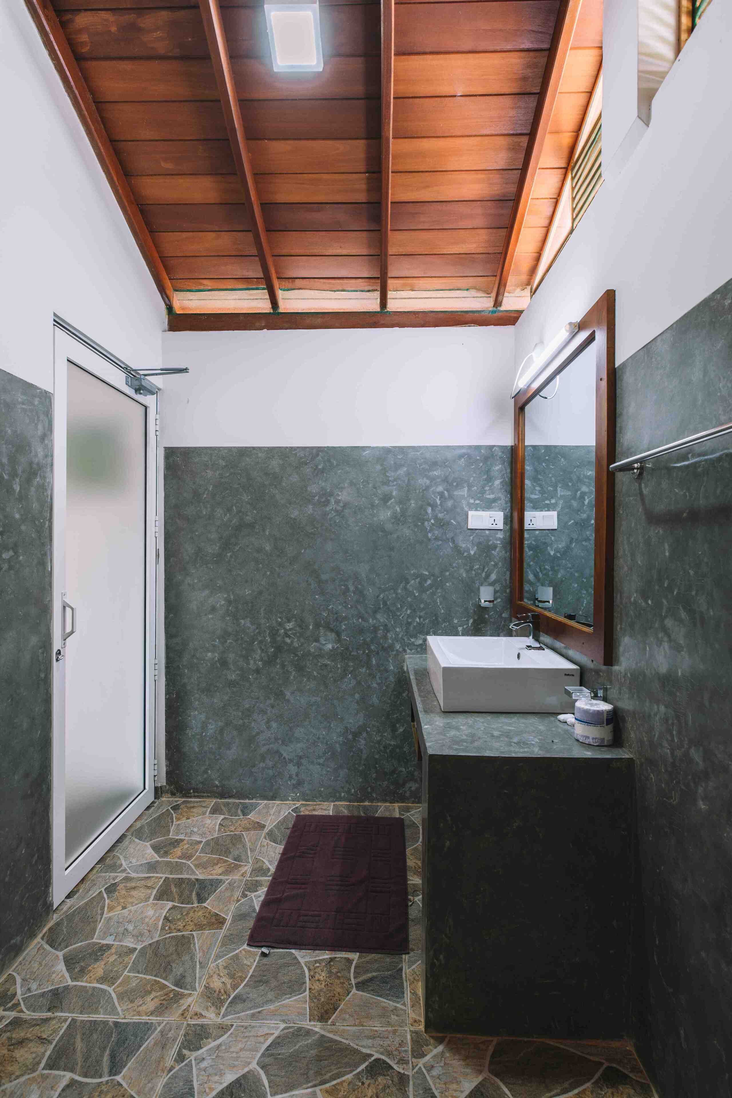 Un baño con suelo de piedra, techo de madera, lavabo y espejo.