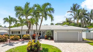 Une maison de plain-pied avec un garage, entourée de palmiers et agrémentée d’un aménagement paysager soigné.