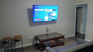 A living room with a mounted TV displaying a menu, a coffee table with a board game, and a couch. - Home Away From Home!!! (Birmingham)