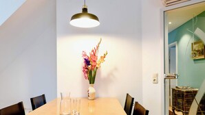Un coin repas avec une table en bois, des chaises noires, un vase de fleurs et un luminaire suspendu.