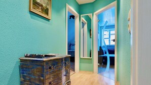 Un couloir aux murs de couleur turquoise, avec un plancher en bois, une commode ancienne et un tableau encadré accroché au mur.