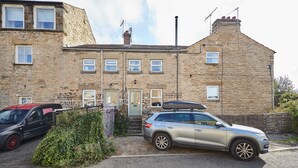 A stone building with multiple windows and a door, a parked car, and a small garden area. - Host Stay Dairy Cottages (Ripon)