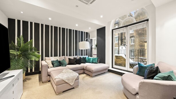 A modern living room with a sectional sofa, a flat-screen TV, and a large window with a view of the city. - Mayfair 3bedr-3batr. 1,405sq/ft balcony A/C (London)