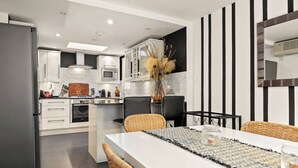 A modern kitchen with white cabinets, a dining area with a white table, wicker chairs, and a decorative vase. - Mayfair 3bedr-3batr. 1,405sq/ft balcony A/C (London)
