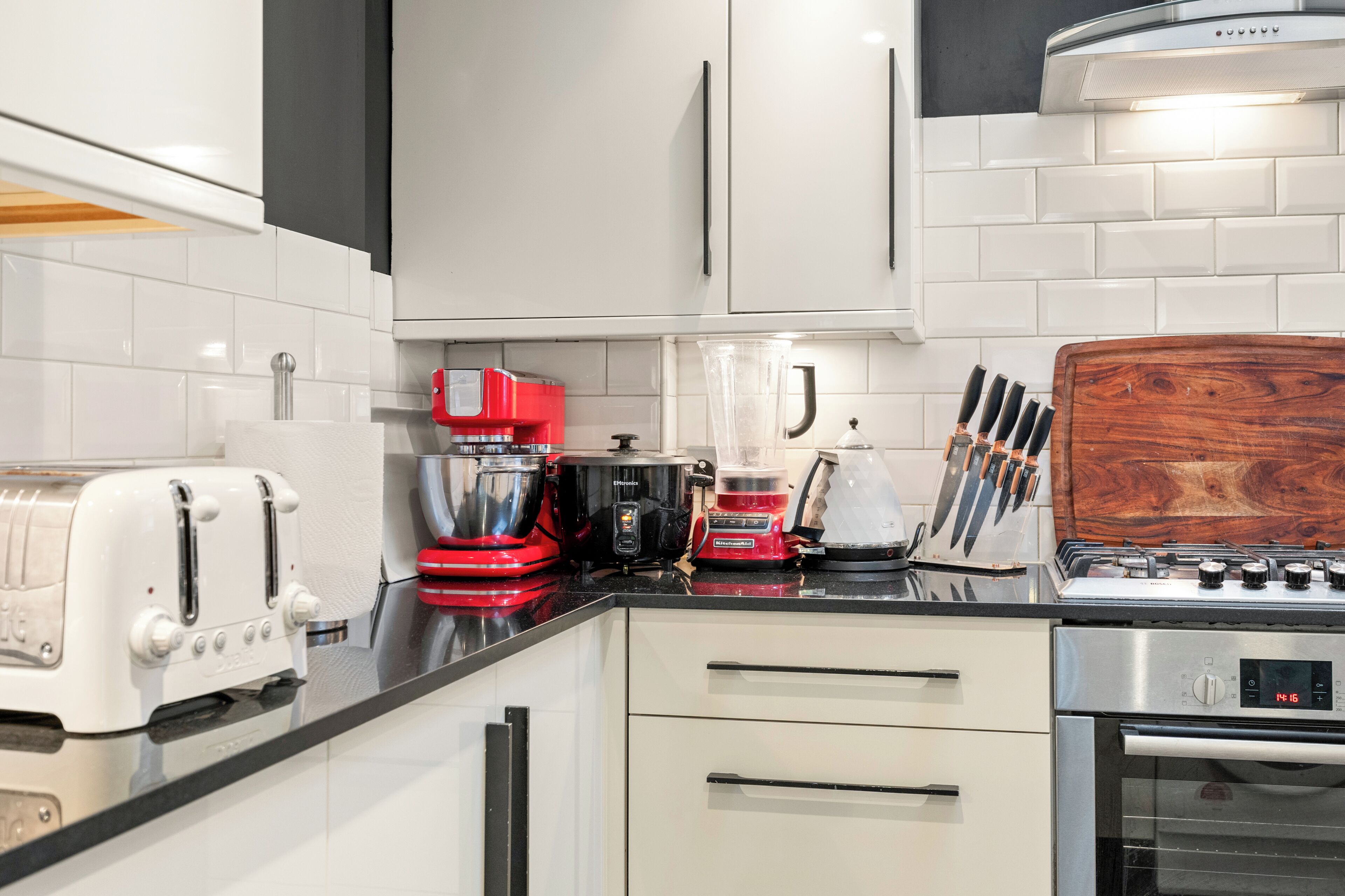A modern kitchen with white cabinets, a red coffee maker, a toaster, and a knife block.