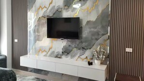 Una sala de estar moderna con una pared de mármol, un televisor de pantalla plana y un mueble blanco para equipo de sonido.