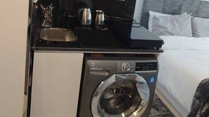 Una kitchenette compacta con microondas, cafetera y lavadora.