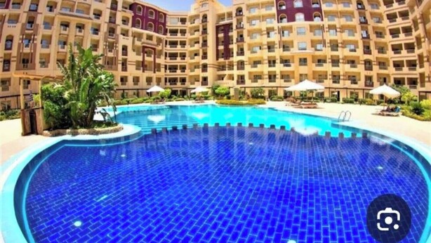 Un hotel con una amplia piscina rodeada de jardines con palmeras y sillas de descanso.